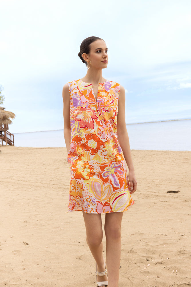 Sleeveless floral linen blend shift dress in orange and pink tones with a split V-neckline, shown on a model standing on a sandy beach.