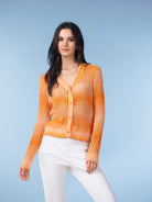 Model wearing a bright orange open-knit V-neck cardigan with button-front closure, styled with light trousers against a blue backdrop.