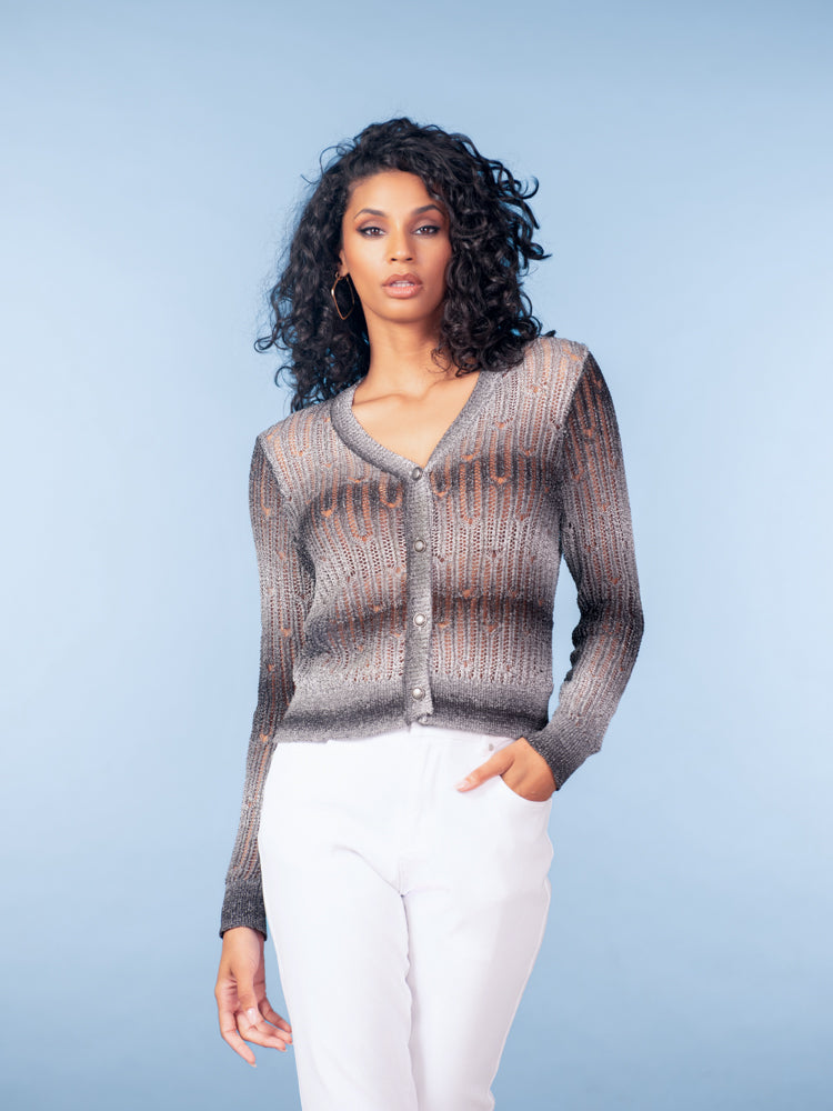 Model wearing a black and grey open-knit V-neck cardigan with button-front closure, styled with light trousers against a soft blue studio background.