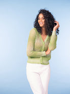 Model wearing a light green open-knit V-neck cardigan with button-front closure, paired with light trousers in a studio setting.