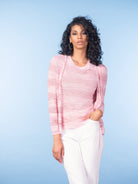 Woman wearing a pink tie-front knit cardigan with matching knit top and white trousers, posed against a soft blue studio background.