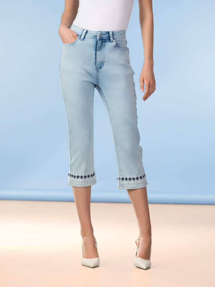 Women’s light wash cropped denim jeans with a slim straight-leg fit, classic five-pocket styling, and embroidered detail along the cuffed hem, shown paired with pointed-toe heels.