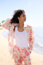 Close-up of model wearing a pink floral sheer blouse layered over a white tank top with matching pink floral pants, styled for a breezy beach look.