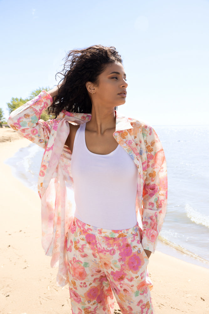 Close-up of model wearing a pink floral sheer blouse layered over a white tank top with matching pink floral pants, styled for a breezy beach look.