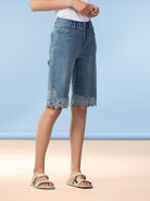Close-up of light wash denim knee-length shorts with scalloped lace hem detail, styled with flat sandals.