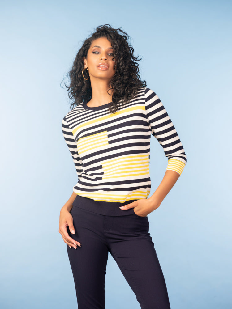 Woman wearing a black, white, and yellow striped cotton sweater with a crew neckline and three-quarter sleeves, paired with black pants, styled against a light blue studio background.