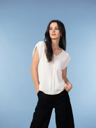 Woman wearing a soft knit cap sleeve sweater with a V-neckline and subtle vertical detailing, paired with wide-leg trousers, styled in a relaxed, modern silhouette against a light blue background.