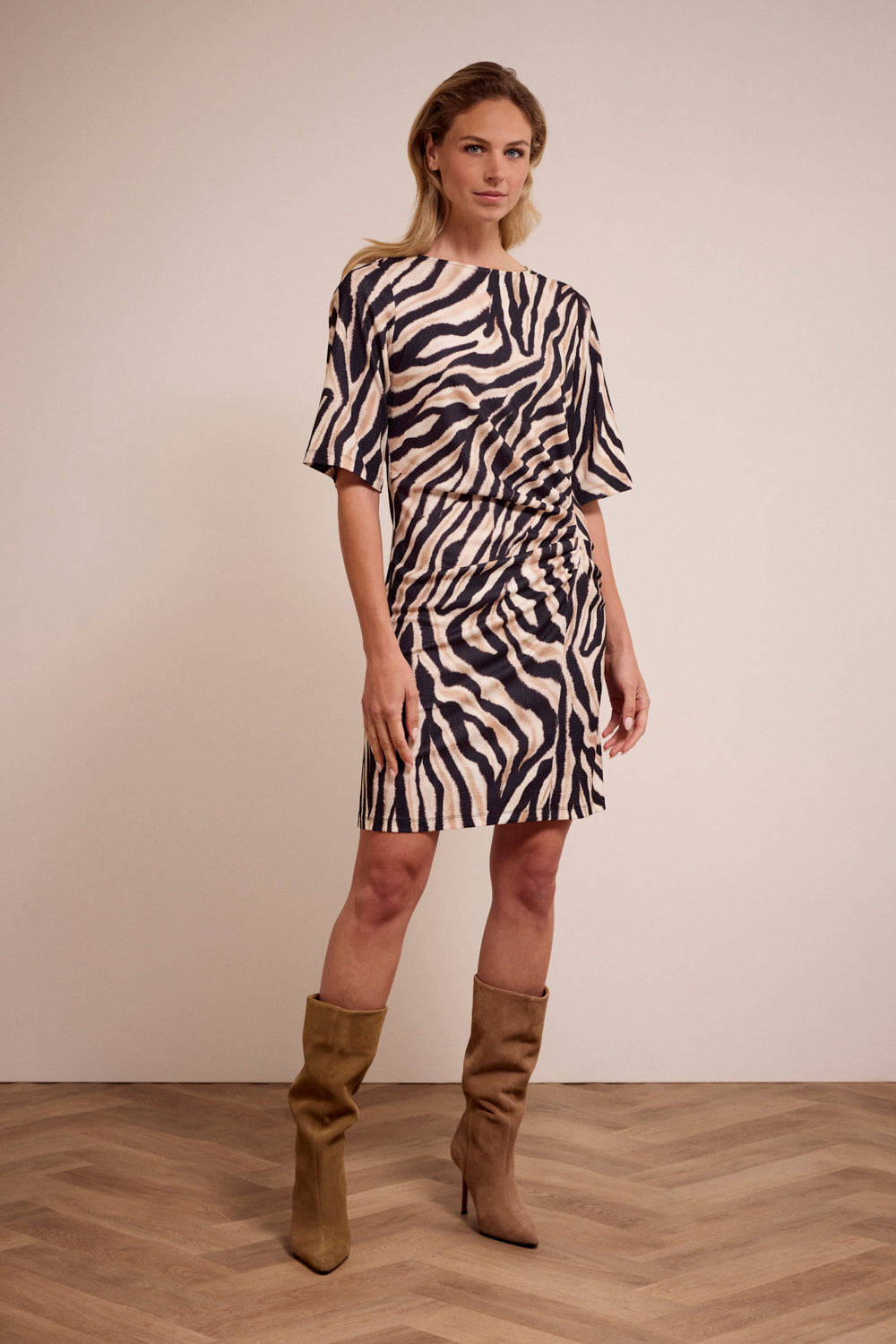 Woman wearing a zebra print dress with brown boots on a plain background