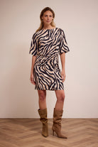 Woman wearing a zebra print dress with brown boots on a plain background