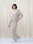 Woman wearing a light gray tracksuit against a white curtain background