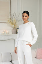 Woman in a white outfit standing in a stylish room with decor elements.