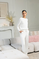 Woman in a white outfit standing in a stylish living room.