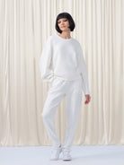 Person wearing a white outfit standing against a white curtain background