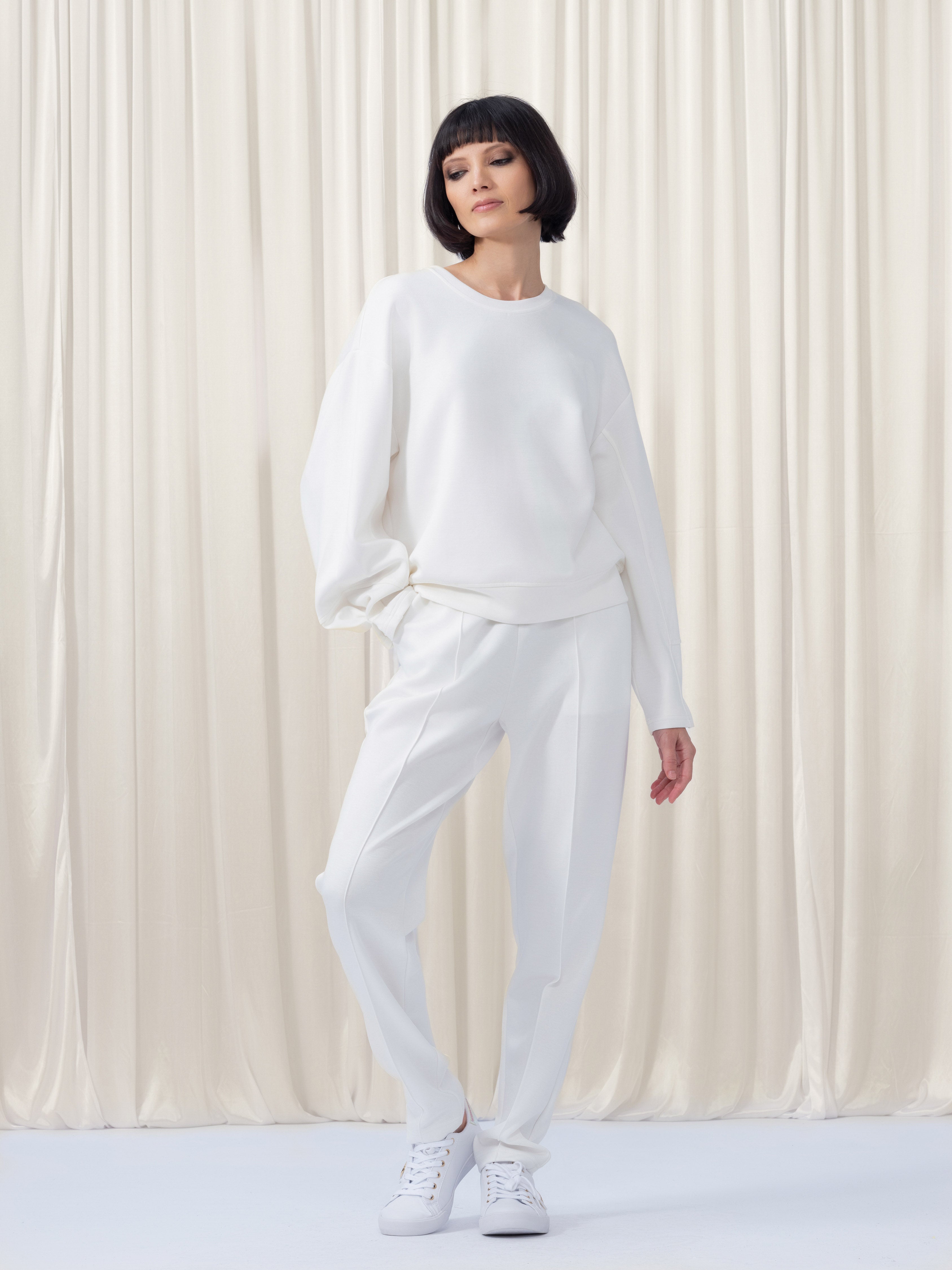 Person wearing a white outfit standing against a white curtain background