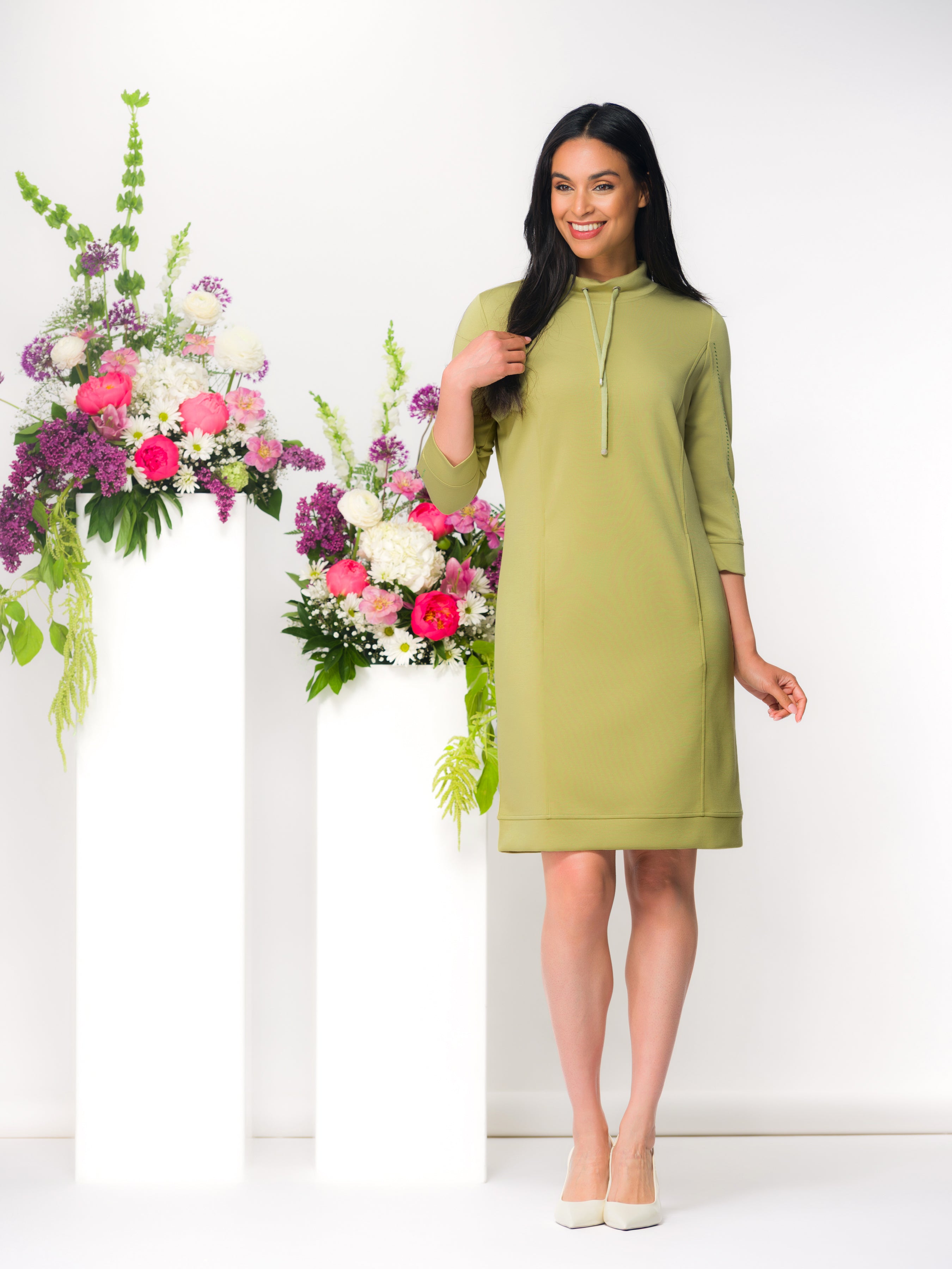 Woman wearing a green dress standing next to floral arrangements on a white background