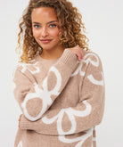 Close-up of a woman wearing a sand patterned crew-neck sweater, highlighting the knit texture, abstract motif, ribbed neckline, and cuffs.