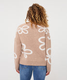 Back view of a woman wearing a sand patterned crew-neck sweater, highlighting the knit texture, abstract motif, ribbed neckline, and cuffs.