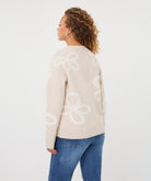 Back biew of a woman wearing a beige patterned crew-neck sweater, highlighting the knit texture, abstract motif, ribbed neckline, and cuffs.