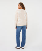 Back view of a woman wearing a beige patterned crew-neck sweater with straight-leg jeans and casual sneakers, shown in a relaxed standing pose against a light studio background.