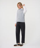 Woman wearing a textured sleeveless sweater vest layered over a collared shirt with straight-leg jeans and sneakers.