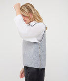 Side view of woman wearing a textured sweater vest with a decorative embellished detail along the side, layered over a collared shirt.