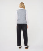 Woman wearing a textured sleeveless sweater vest layered over a collared shirt with straight-leg jeans and sneakers.