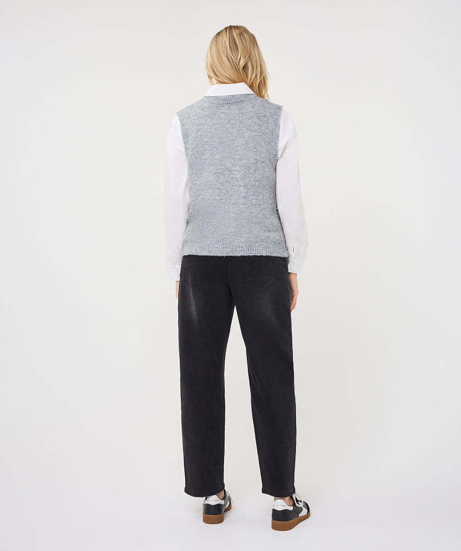Woman wearing a textured sleeveless sweater vest layered over a collared shirt with straight-leg jeans and sneakers.