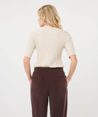 Woman modelling an ivory ribbed knit short-sleeve top with a high neckline and fitted silhouette, shown from the back.