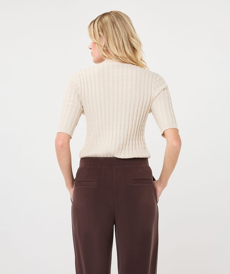 Woman modelling an ivory ribbed knit short-sleeve top with a high neckline and fitted silhouette, shown from the back.