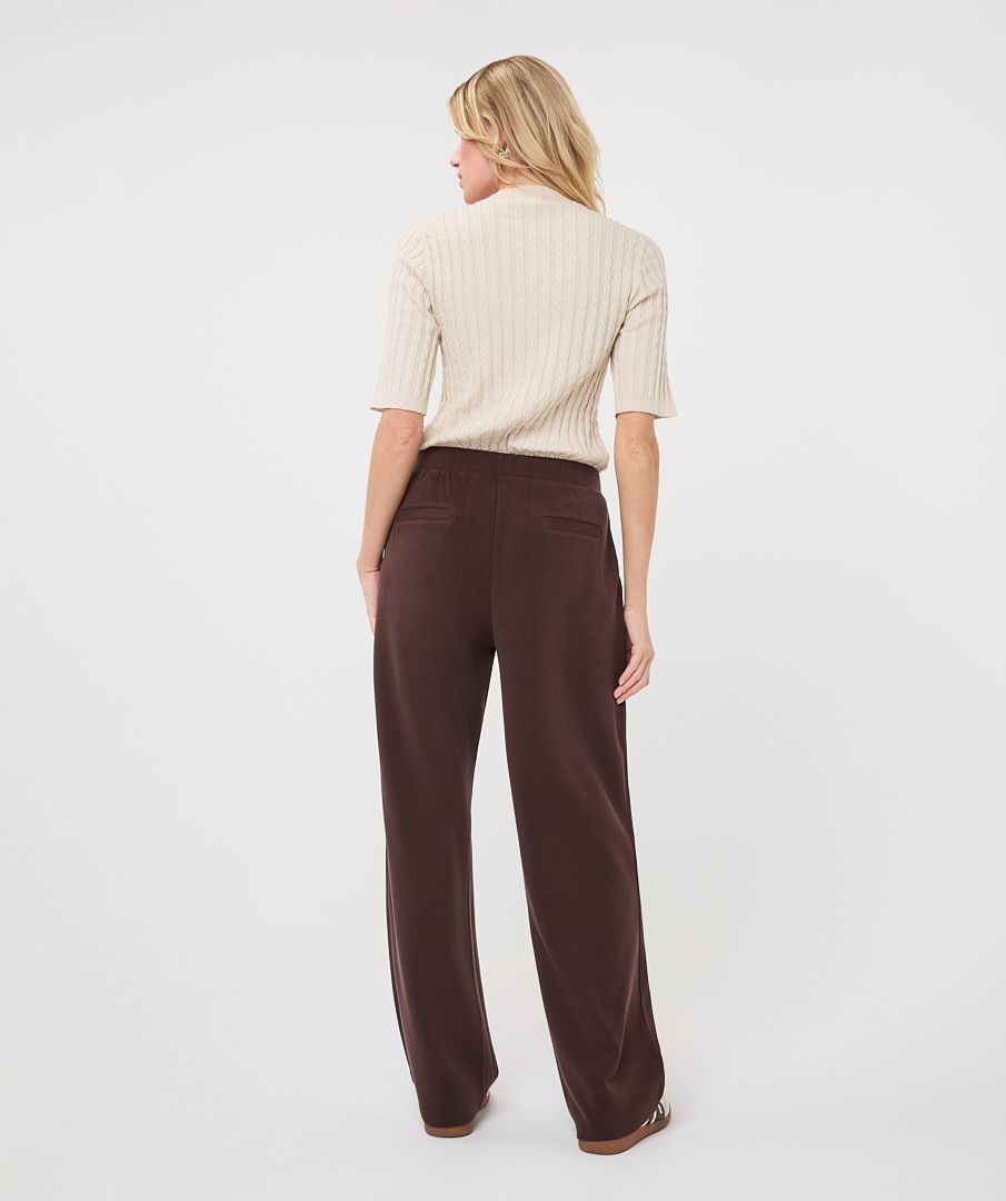 Woman modelling an ivory ribbed knit short-sleeve top with a high neckline and fitted silhouette, shown from the back.