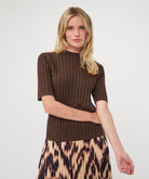 Woman modelling a brown ribbed knit short-sleeve top with a high neckline and fitted silhouette, paired with a printed skirt.