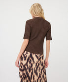 Woman modelling a brown ribbed knit short-sleeve top with a high neckline and fitted silhouette, shown from the back, paired with a printed skirt.