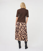 Woman modelling a brown ribbed knit short-sleeve top with a high neckline and fitted silhouette, shown from the back, paired with a printed skirt.