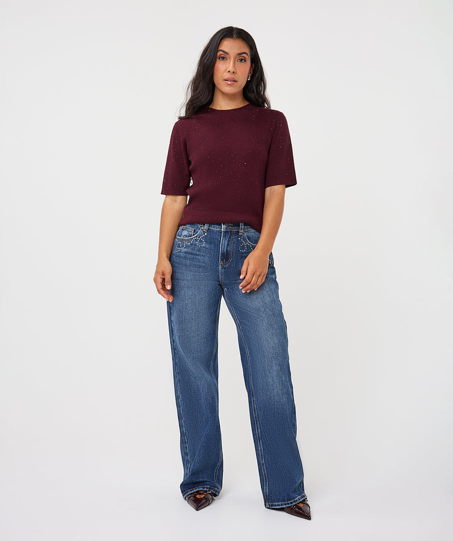 woman wearing a burgundy ribbed knit top with subtle sparkle detailing and blue wide-leg jeans