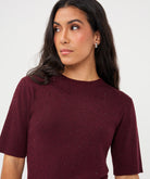 Front close-up of a woman wearing a burgundy ribbed knit top with subtle sparkle detailing and a crew neckline.