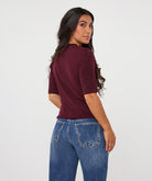 Back three-quarter view of a woman wearing a burgundy ribbed knit top with subtle sparkle detailing and blue wide-leg jeans.