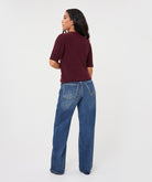Full back view of a woman wearing a burgundy ribbed knit top with subtle sparkle detailing and blue wide-leg jeans.