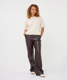 Woman wearing the cream Rosalie Lace Top with dark brown leather-look wide-leg trousers and casual sneakers, front view.