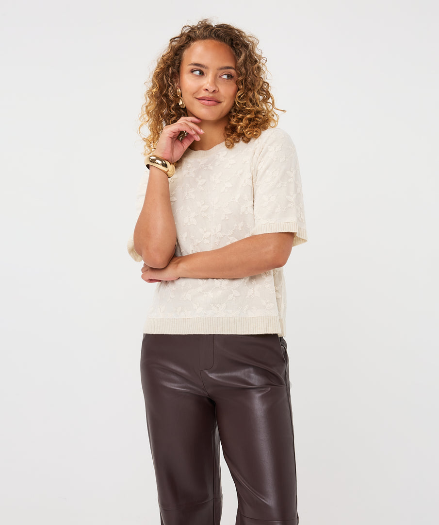 Woman wearing the cream Rosalie Lace Top with dark brown leather-look wide-leg trousers