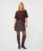 Woman wearing the brown Rosalie Lace Top with a leather-look wrap skirt and knee-high boots, front view.