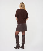 Woman wearing the brown Rosalie Lace Top with a leather-look wrap skirt and knee-high boots