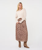 Woman wearing the Elara Crinkle Midi Skirt in taupe with a cream long-sleeve sweater and taupe ankle boots, showing the full flowing midi silhouette.