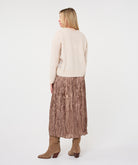 Woman wearing the Elara Crinkle Midi Skirt in taupe with a cream long-sleeve sweater and taupe ankle boots, showing the full flowing midi silhouette.
