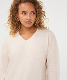 Woman wearing an ivory V-neck sweater with long sleeves and a relaxed fit