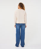 Woman wearing an ivory V-neck sweater with long sleeves and a relaxed fit, paired with blue jeans.