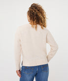 Woman wearing an ivory V-neck sweater with long sleeves and a relaxed fit, paired with blue jeans.