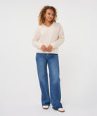 Woman wearing an ivory V-neck sweater with long sleeves and a relaxed fit, paired with blue jeans.