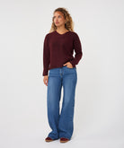 Woman wearing a burgundy V-neck sweater with long sleeves and a relaxed fit, paired with wide-leg blue jeans.