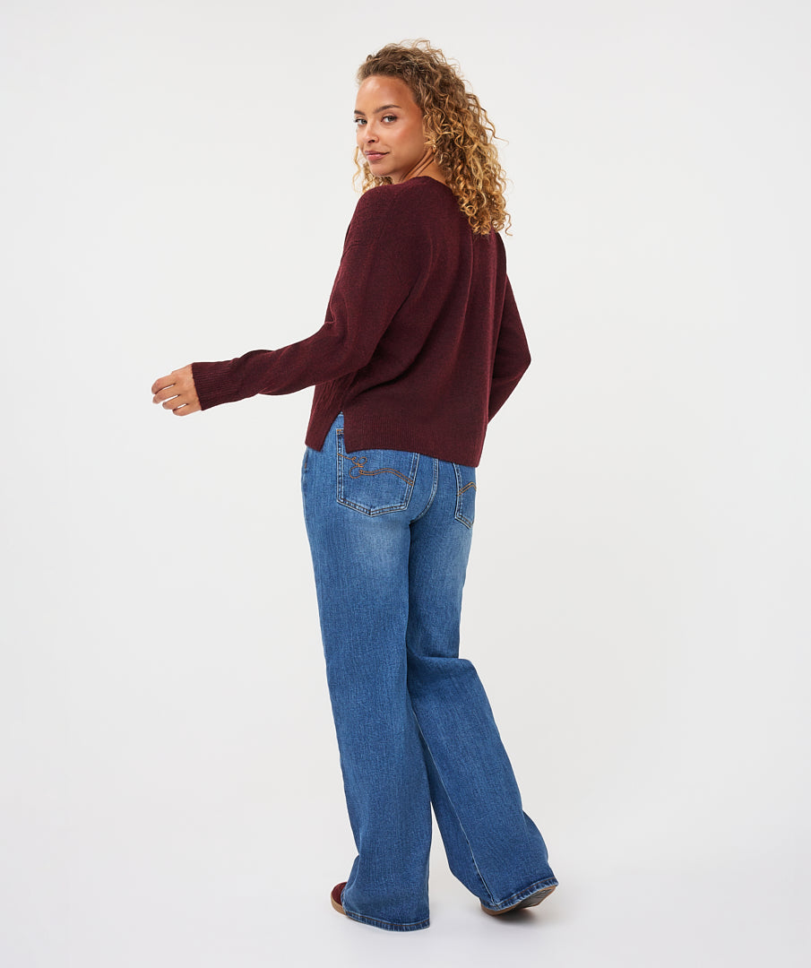Woman wearing a burgundy V-neck sweater with long sleeves and a relaxed fit, paired with wide-leg blue jeans.