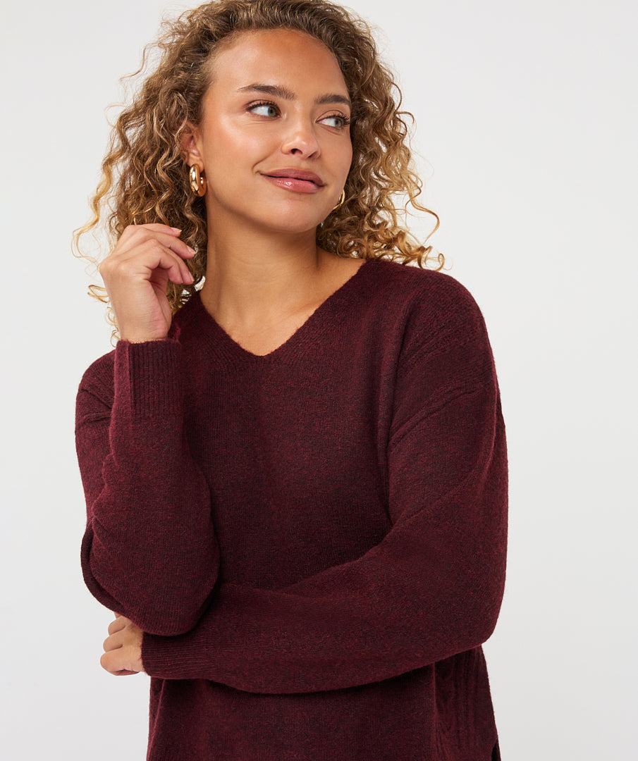 Woman wearing a burgundy V-neck sweater with long sleeves and a relaxed fit